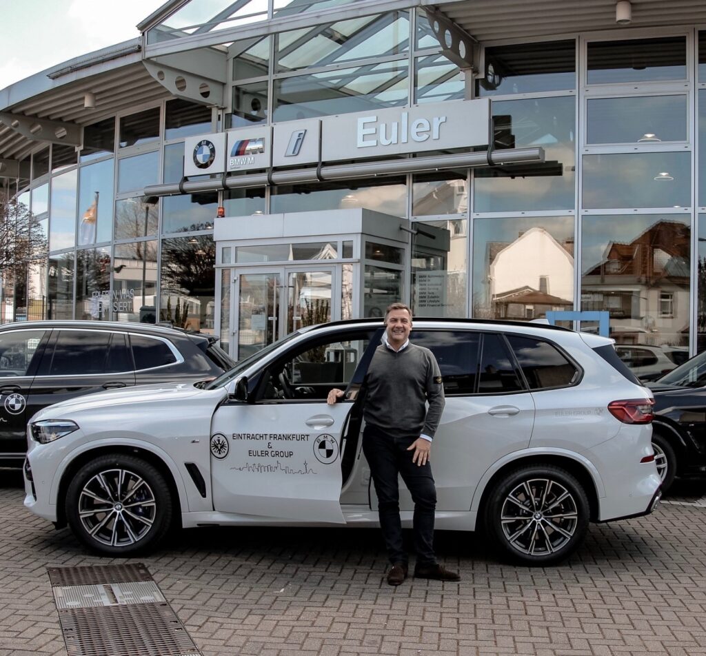 Freiherr Cyril von Recum vor einem der drei Fahrzeuge aus dem Hause BMW EULER, die aktuell für besonders gefährdete Eintracht-Mitglieder auf den Straßen Frankfurts unterwegs sind.